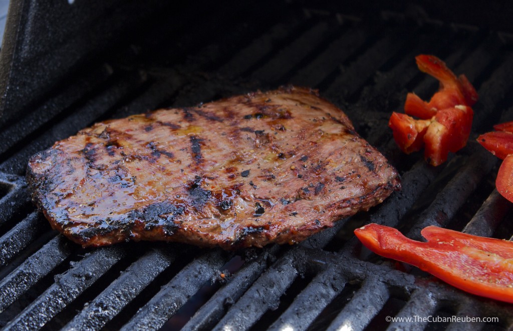 Marinated flank steak sizzling on the grill with bell pepper pieces.